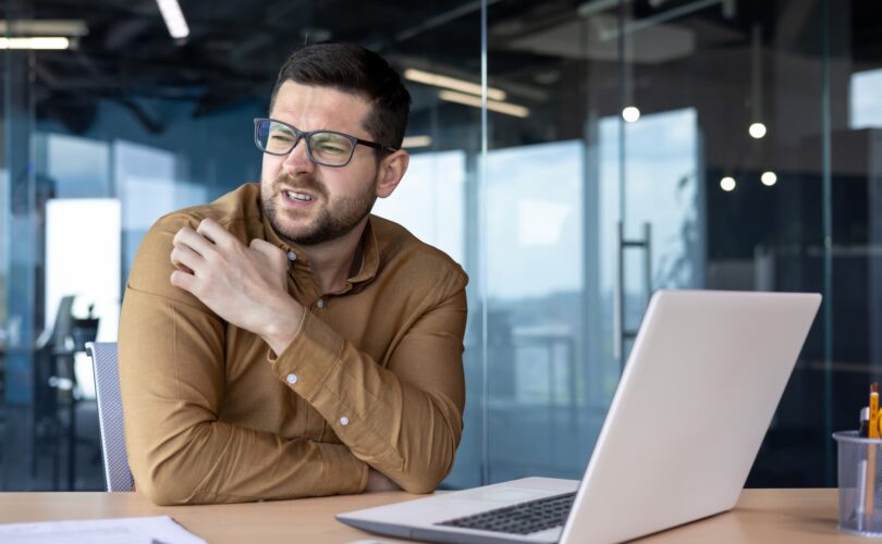 A young man works in the office on a laptop with documents. Feels an allergic reaction, itching and
