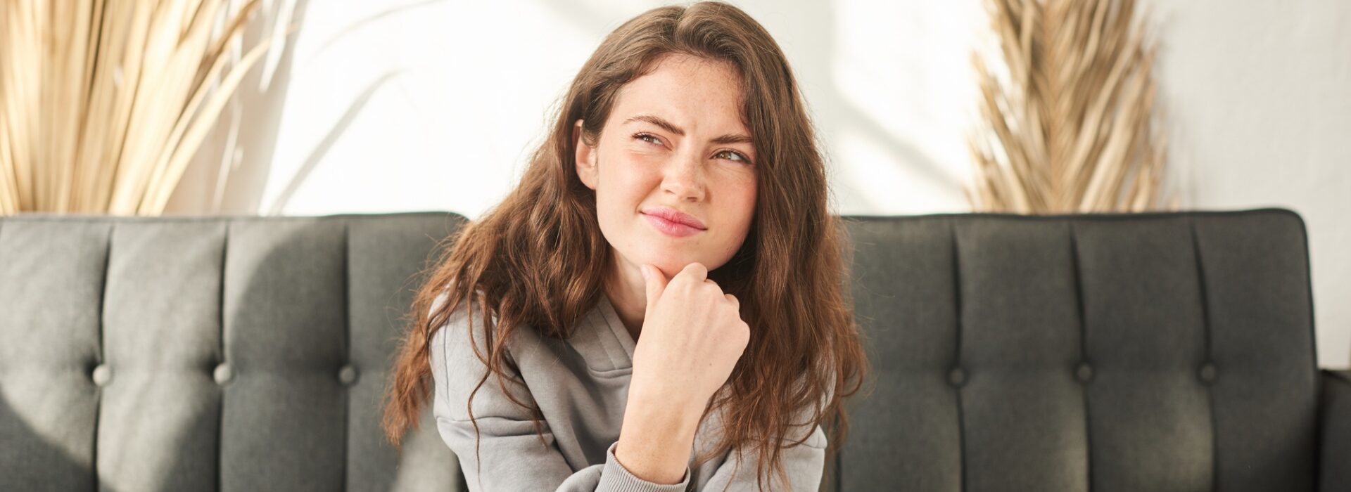 young woman sits on couch discomfort and squints. bored and sad woman with no mood