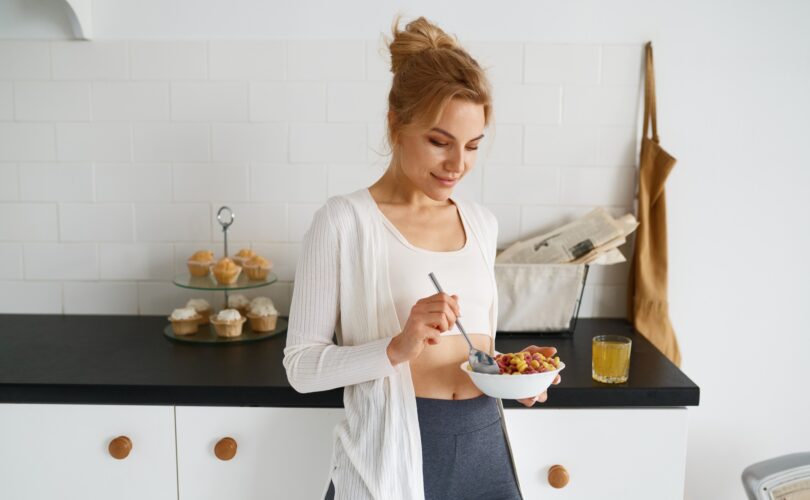 Dreamy young woman eating cereals with milk on home kitchen