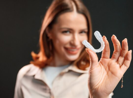 Young woman is standing against black background and holding aligner